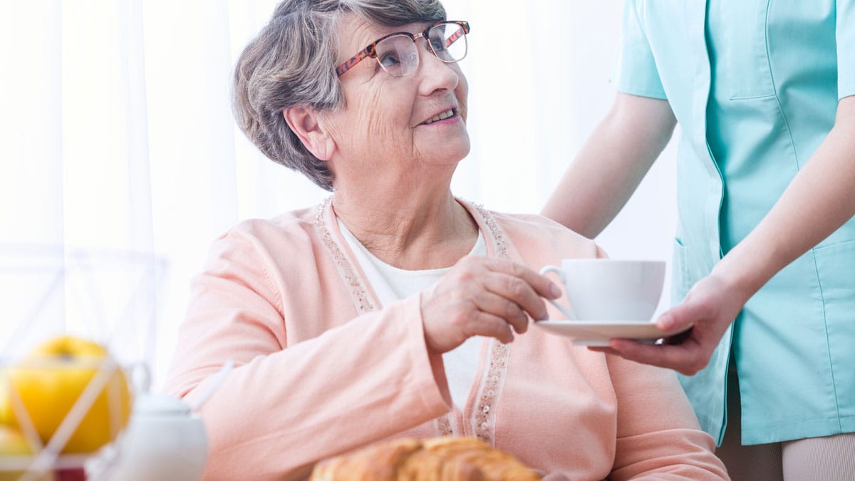 Bild Pflegerin reicht einer älteren Patientin eine Tasse mit einem Heißgetränk
