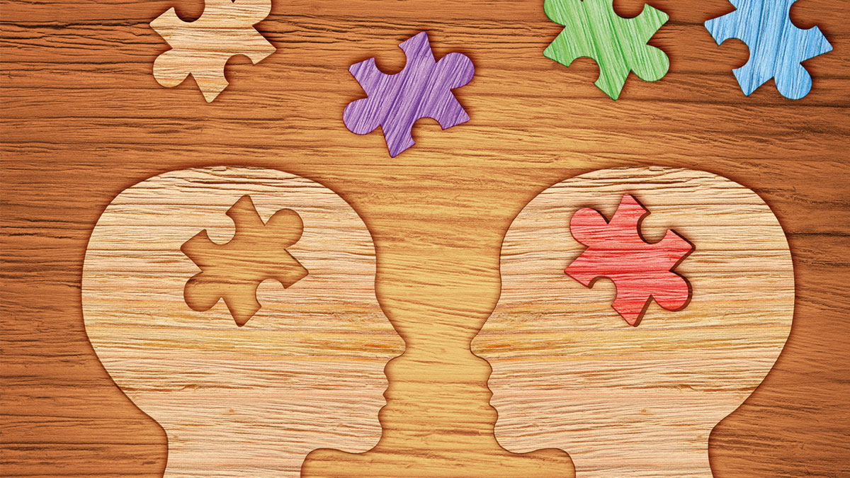 Bild Auf einem Holzbrett sieht man zwei Kopfsilhouetten mit Puzzle teilen